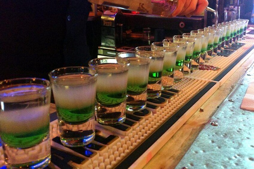 A bar with shot glasses filled with green liquid, arranged on a wooden bar. 4