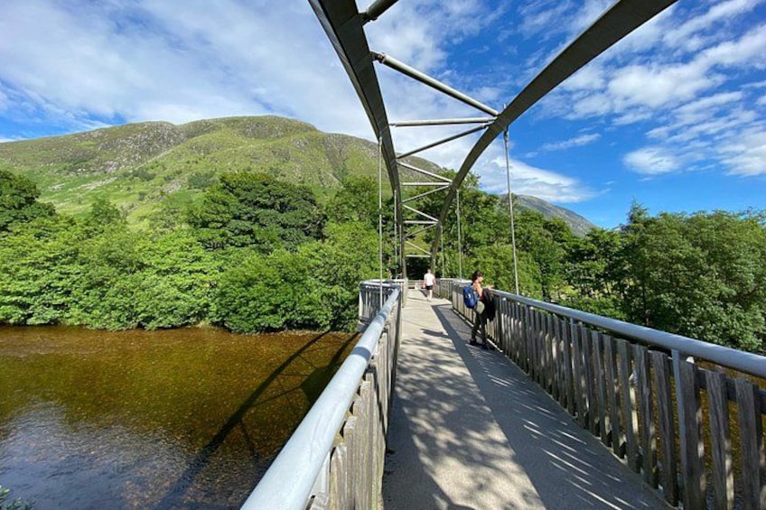 A pedestrian bridge over a river with greenery and hills in the background. 3