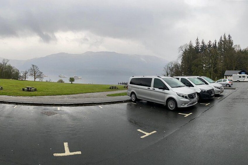 A parking lot with several parked vehicles, a grassy area, and a mountainous landscape in the background. 2