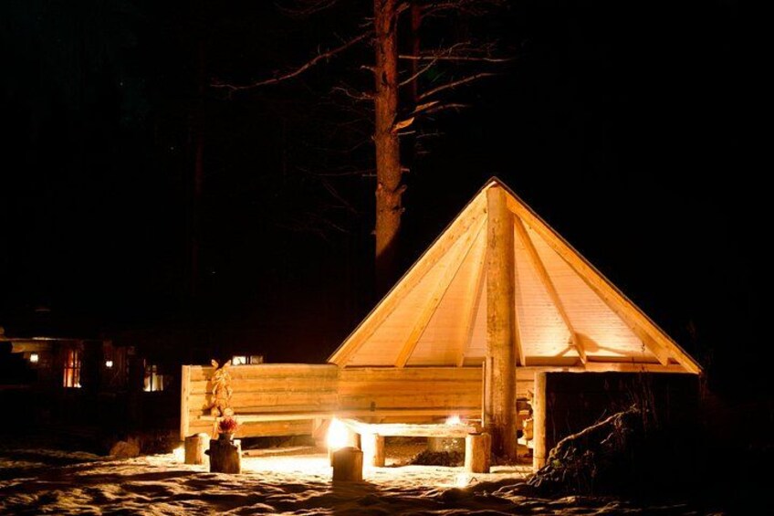A wooden cabin with a triangular roof illuminated by lights at night. 3