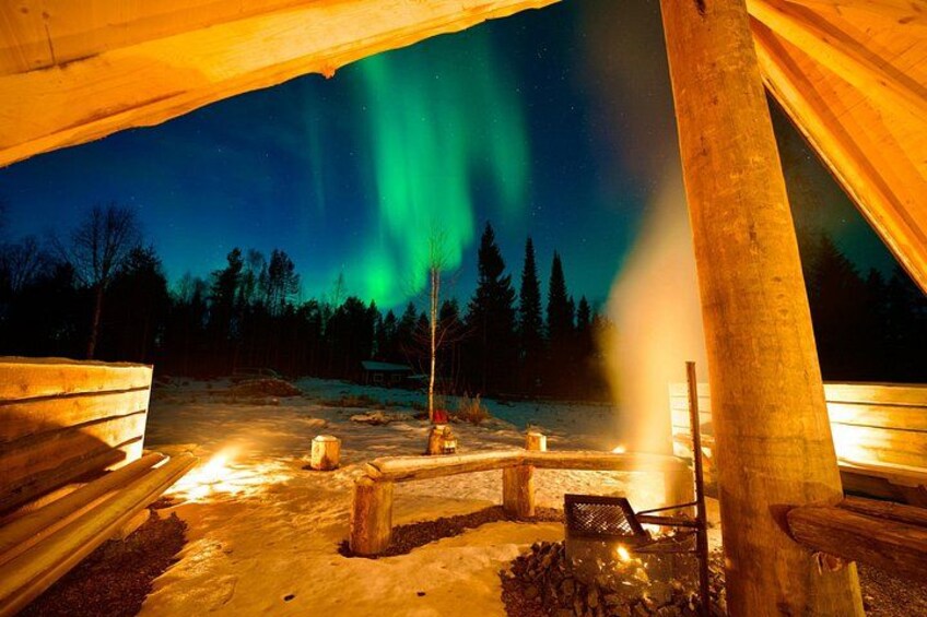 A wooden structure with a view of the night sky, aurora borealis, and a snowy landscape. 5
