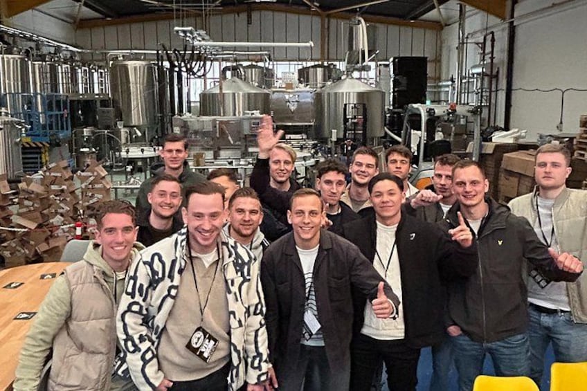 A group of people in a brewery with stainless steel tanks and equipment. 2