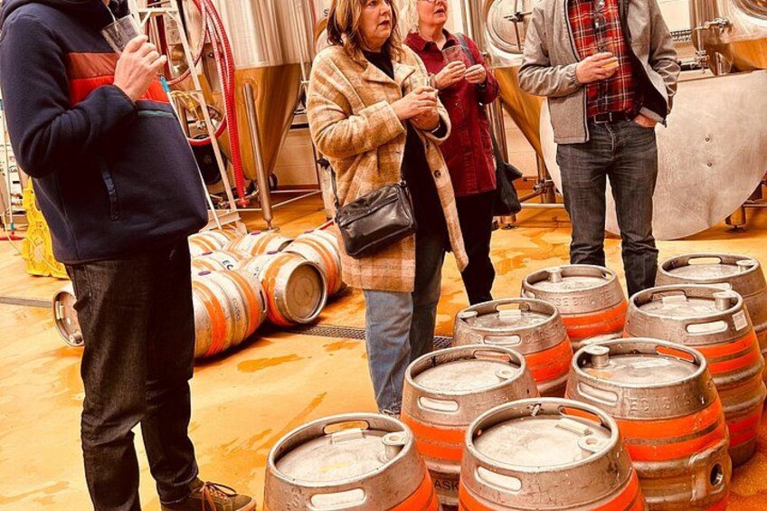 People standing around large metal barrels in a room with industrial equipment. 2