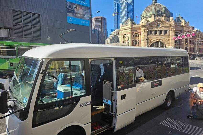 A white bus with its door open, parked on a city street with buildings and a large dome structure in the background. 2