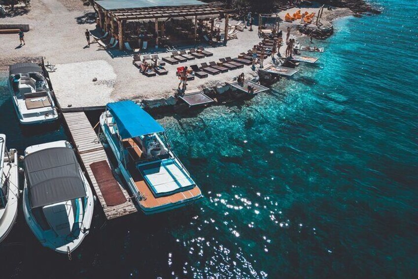 Un muelle con barcos amarrados, una zona de playa con sombrillas y agua cristalina azul. 4