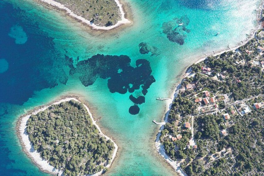 An aerial view of a coastal area with clear turquoise waters, several small islands, and a densely populated peninsula with buildings. 1