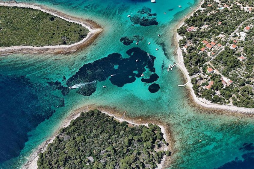 An aerial view of a coastal area with clear turquoise waters, a small island with dense vegetation, and a nearby town with buildings and roads. 2