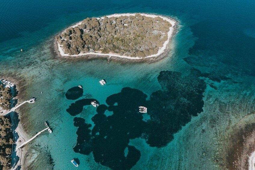 An aerial view of a coastal area with a small island, clear blue waters, and several boats. 3
