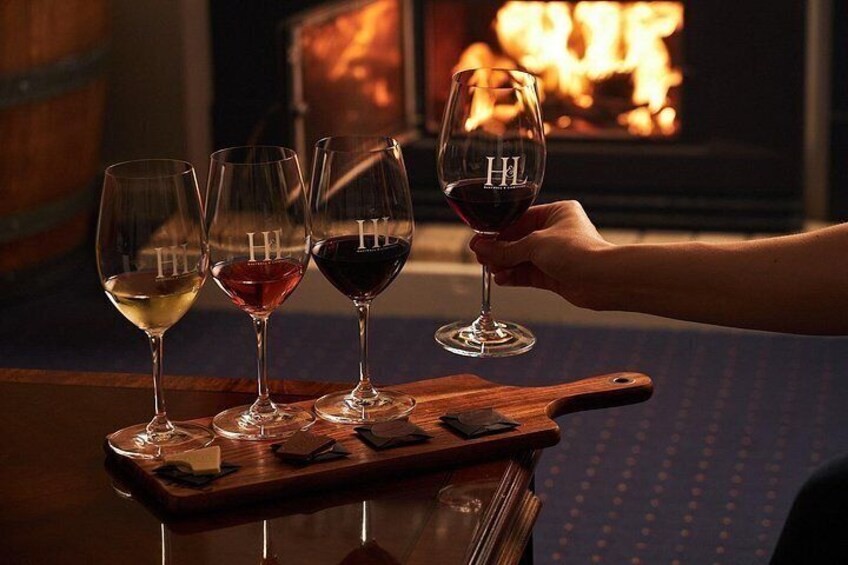 A wooden tray with four wine glasses, one held by a person, and a fireplace in the background. 4