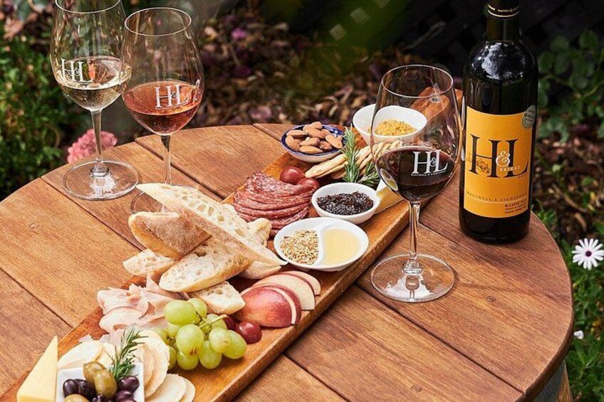 Una mesa de madera con una tabla de embutidos, copas de vino y una botella de vino. 2