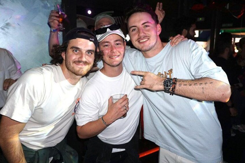 Three people in a casual setting, possibly a party or social event, with one person wearing a white t-shirt and another with a watch and bracelets. 4