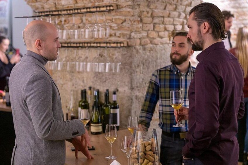 A social gathering with people holding glasses of wine, a stone wall, and bottles of wine on a table. 2