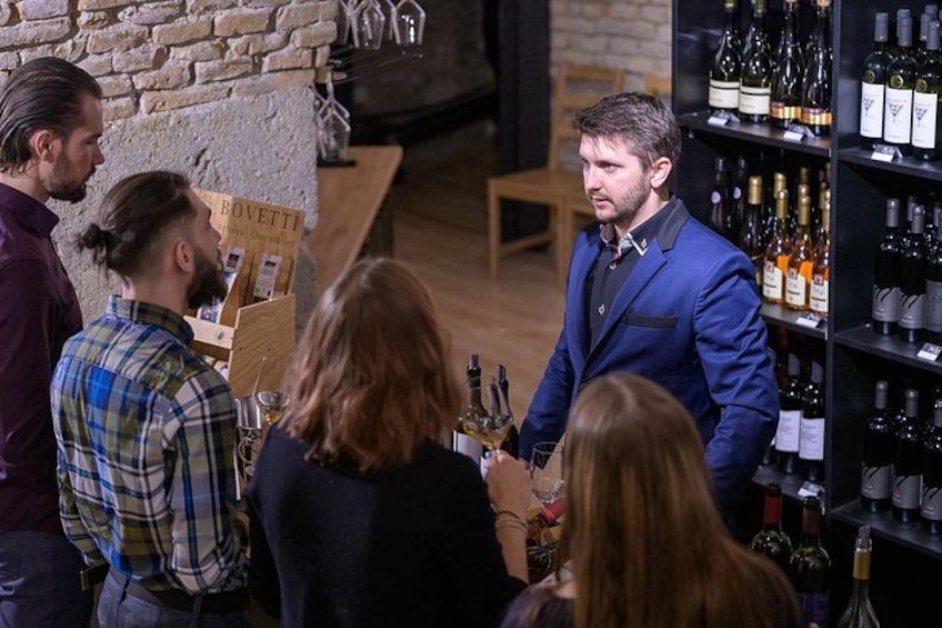 Un bar où l’on voit un homme en costume bleu servir des boissons, entouré d’étagères remplies de bouteilles de vin. 3