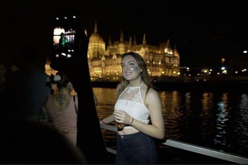 A person holding a drink, a boat, and a historic building in the background. 2