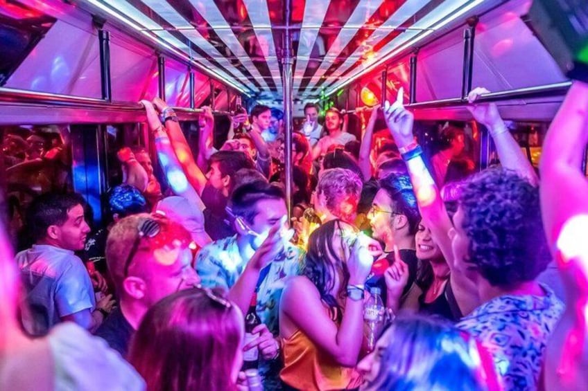 Interior de un tren abarrotado, con gente sosteniendo bebidas y levantando las manos. 2