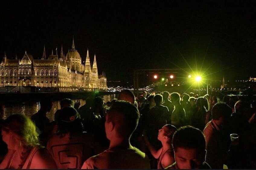 A crowd of people gathered near a historic building with a large dome and spires, under a night sky with a bright light source in the distance. 3