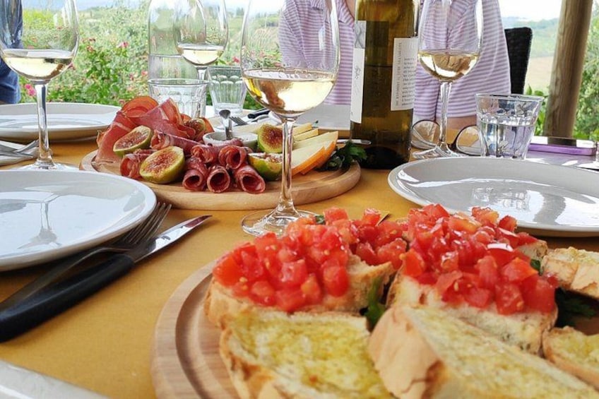 A table with food and wine, including a plate of sliced bread topped with tomatoes, a plate of prosciutto and figs, and a bottle of wine. 2