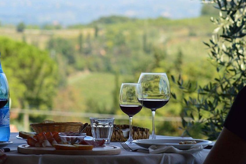 A table set with wine glasses, a basket, and a plate of food, overlooking a scenic landscape. 1