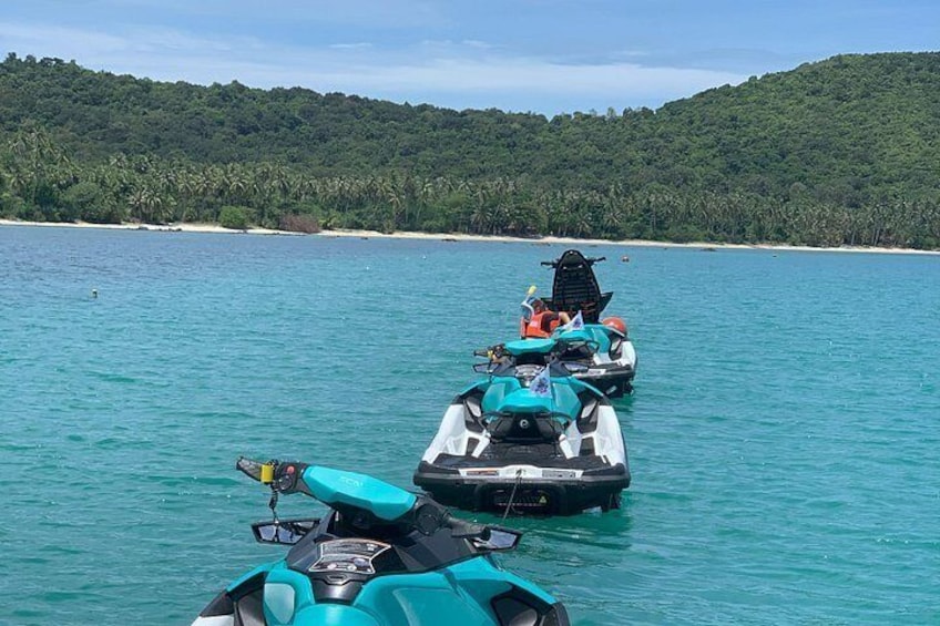 Tre jetski på roligt turkis vand med en skovklædt ø i baggrunden. 5