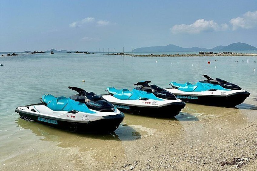 Tre Sea-Doo jetski på en sandstrand med roligt vand og fjerne bjerge. 4