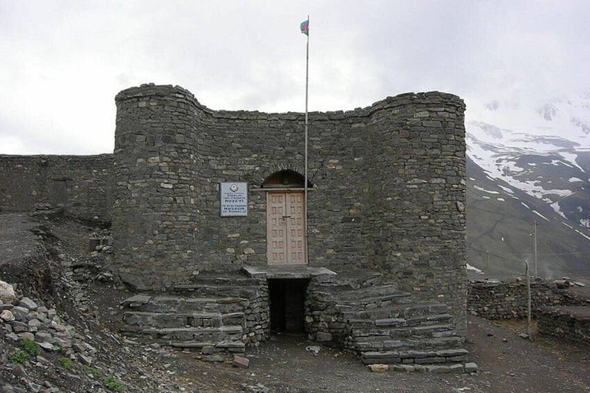 Een gebouw van steen met een vlag, een houten deur en een bord. 5