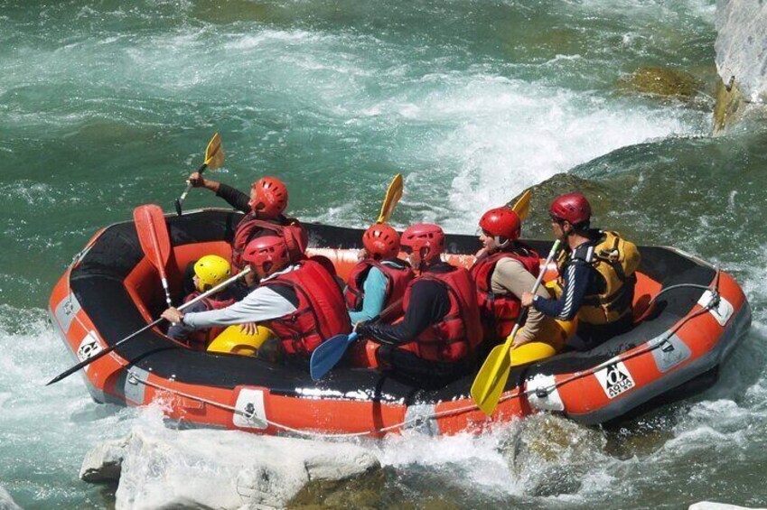 A group of people in a small inflatable raft navigating through a river with rapids. 1