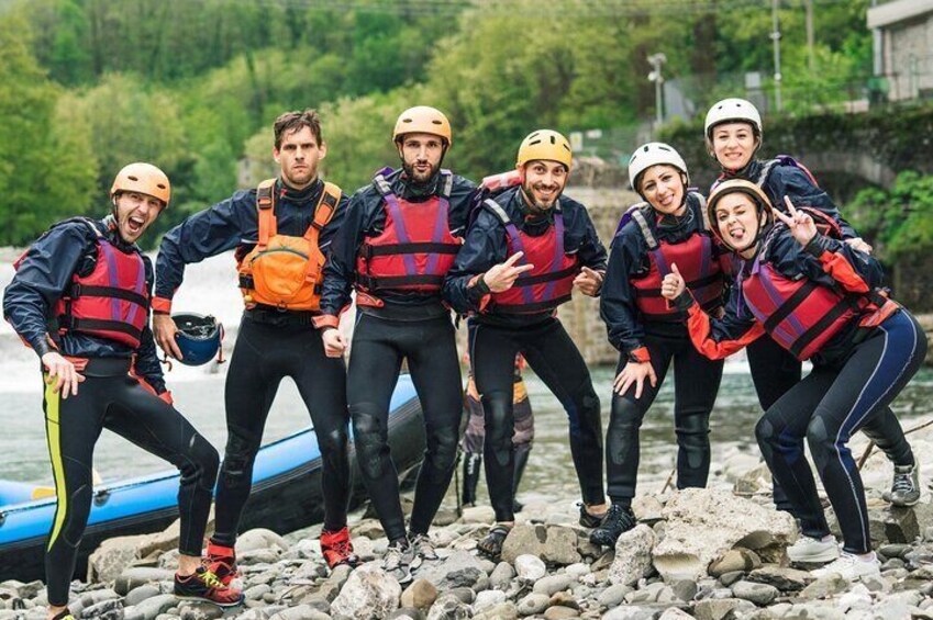 A group of people in life jackets and helmets by a rocky riverbank. 1