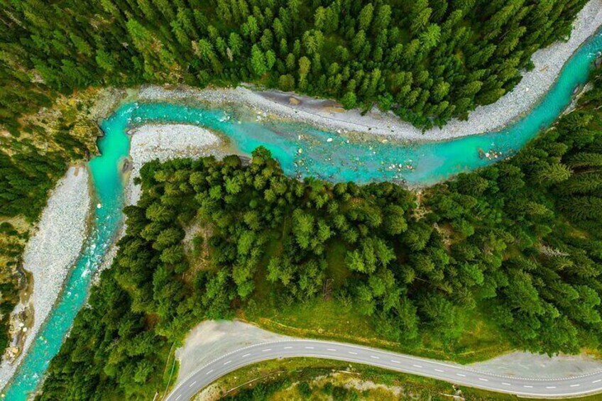 An aerial view of a turquoise river winding through a forested area with a winding road alongside. 5