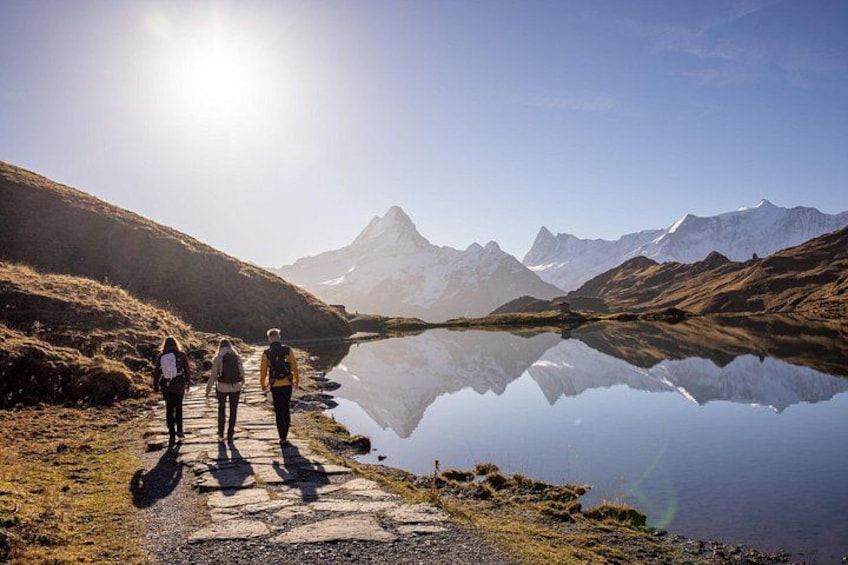Un grupo de personas caminando por un sendero junto a un lago tranquilo con montañas al fondo. 2