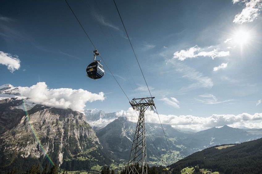 A cable car suspended above a mountainous landscape with a clear sky and a sun shining. 4
