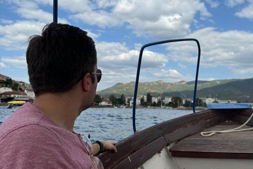 Una persona en un barco, con vista a un lago, edificios y montañas al fondo. 4
