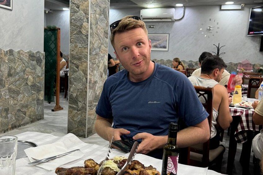 Un hombre sentado a una mesa con comida, una botella de vino y un vaso de agua. 5