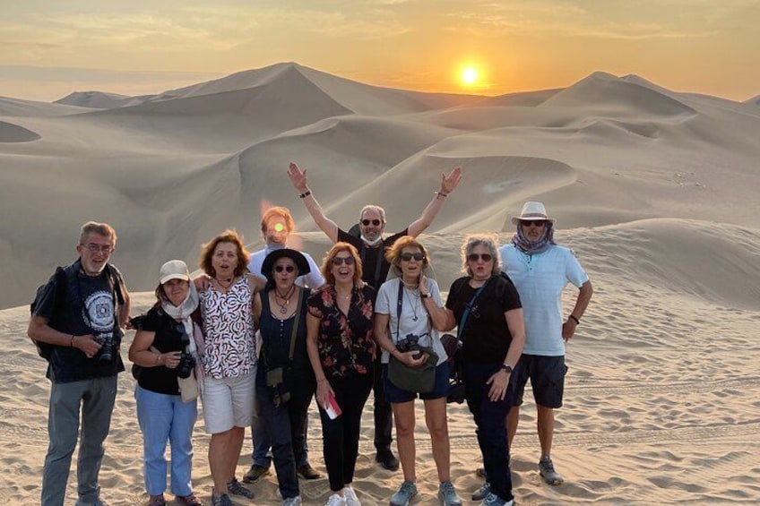 A group of people standing on a sand dune with the sun setting in the background. 3