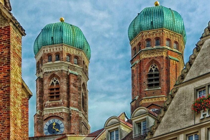 Two historic towers with green domes and a clock face, surrounded by buildings. 2