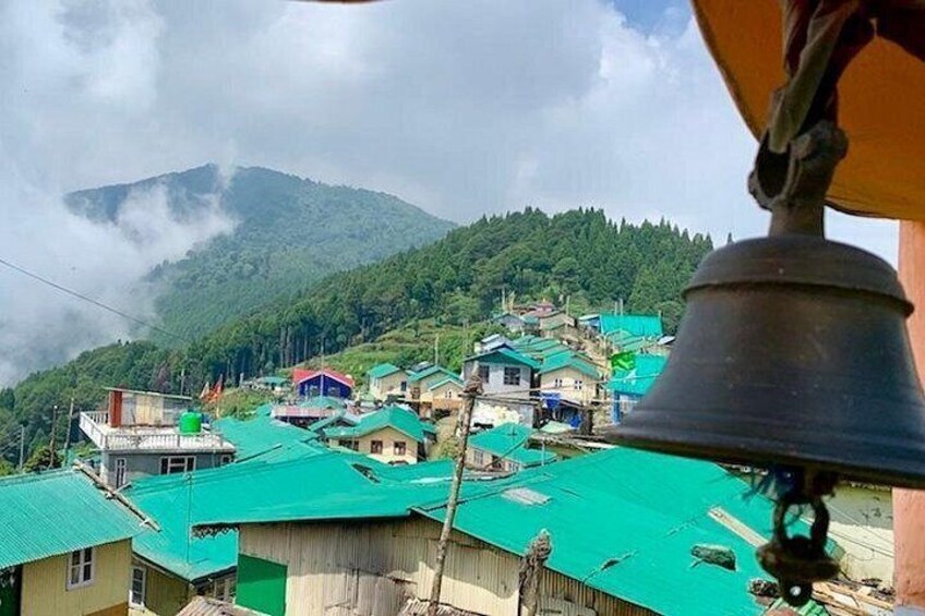 A village with green-roofed buildings, a bell, and a mountain in the background. 5