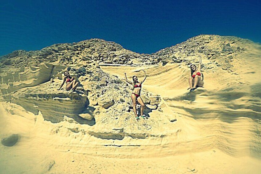 A desert landscape with sand dunes and three individuals in bikinis. 4