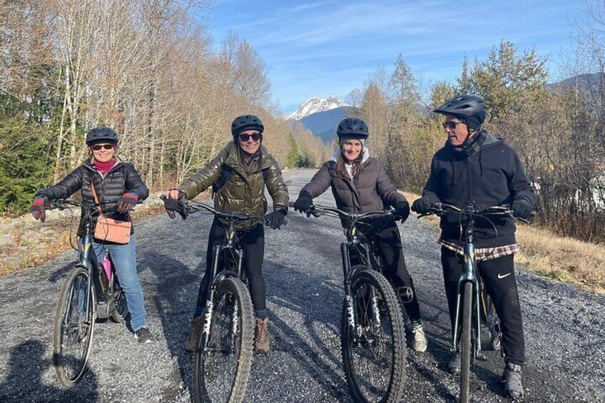 Quatre personnes à vélo sur un chemin de gravier, avec des arbres et des montagnes en arrière-plan. 3