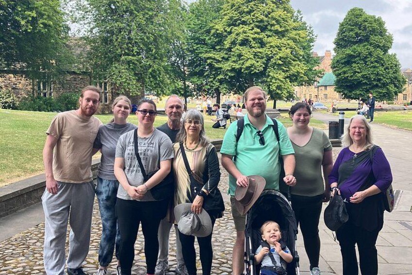 A group of people standing on a stone pathway in a park with trees and a building in the background. 5