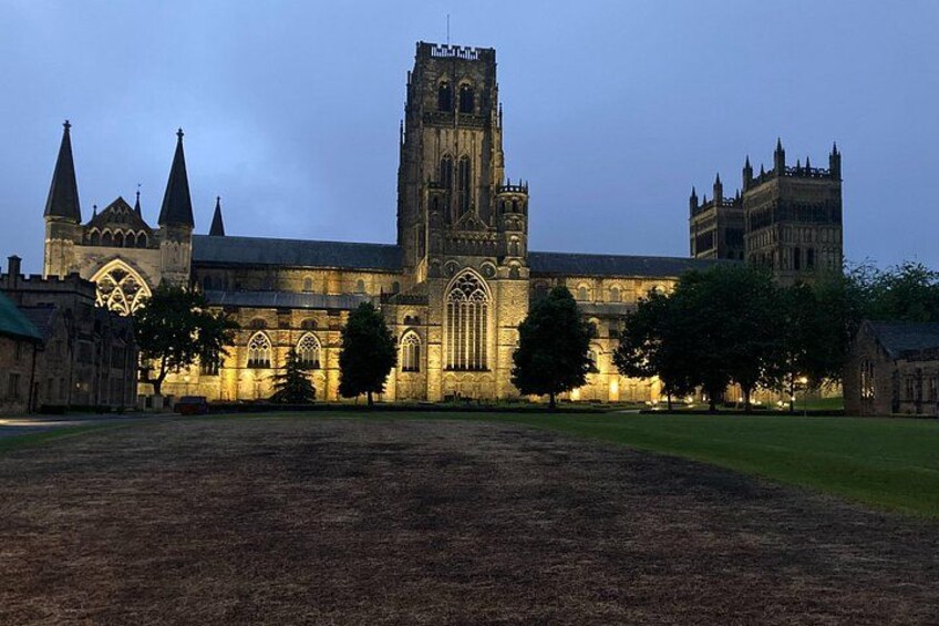 A large, illuminated cathedral with a prominent tower and multiple spires, surrounded by a grassy field and trees. 3