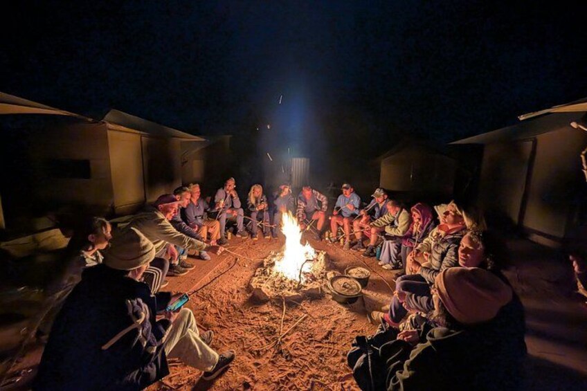 A group of people sitting around a campfire at night. 2