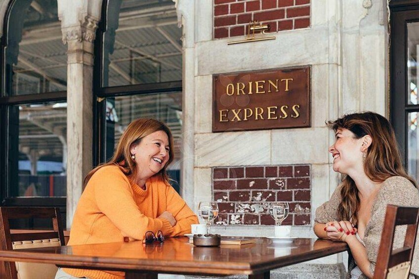 Dos personas sentadas en una mesa en un restaurante, con un letrero en la pared que dice 'ORIENT EXPRESS'. 5