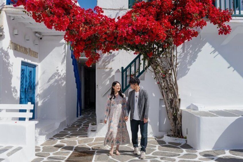 A couple walking on a white-washed street with red flowers and blue doors. 1