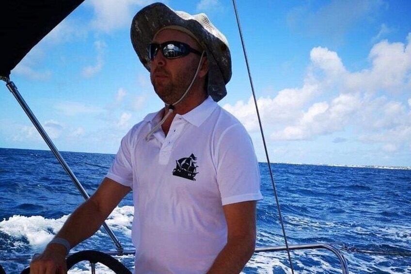 A person on a boat with a white shirt and a logo, steering the boat on the water. 2