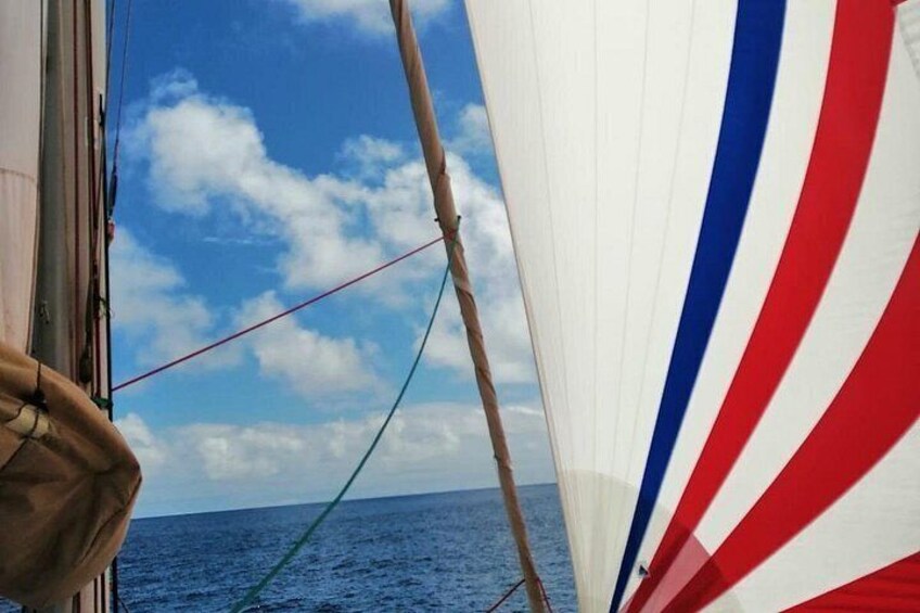 A sailboat with a white sail featuring red and blue stripes, a clear blue sky, and calm ocean water. 3