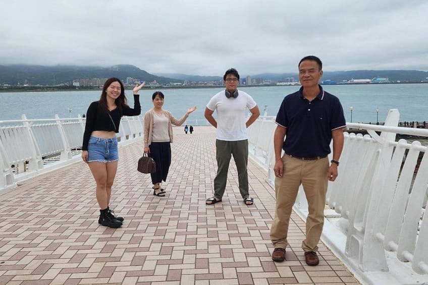 A group of people on a brick-paved promenade with a body of water and mountains in the background. 2