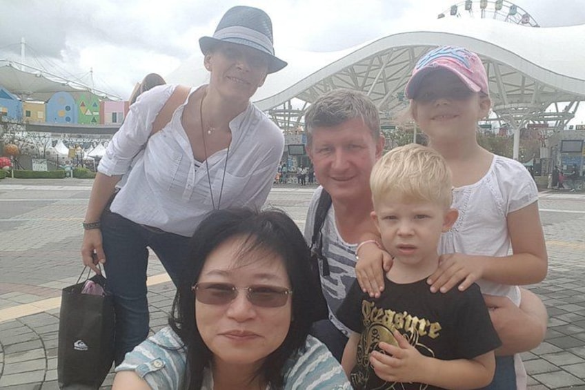 A family of five at an outdoor amusement park with a large white canopy structure in the background. 2