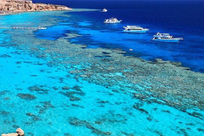 A coastal area with clear turquoise waters, rocky seabed, and several boats. 1