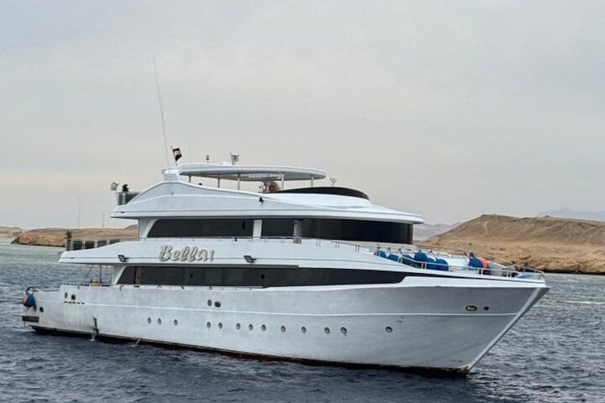 A large white yacht named 'Bella' on calm waters with a hilly landscape in the background. 4