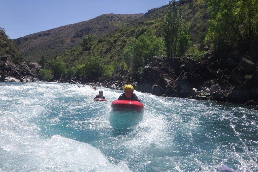 Two people rafting on a river surrounded by greenery and hills. 5
