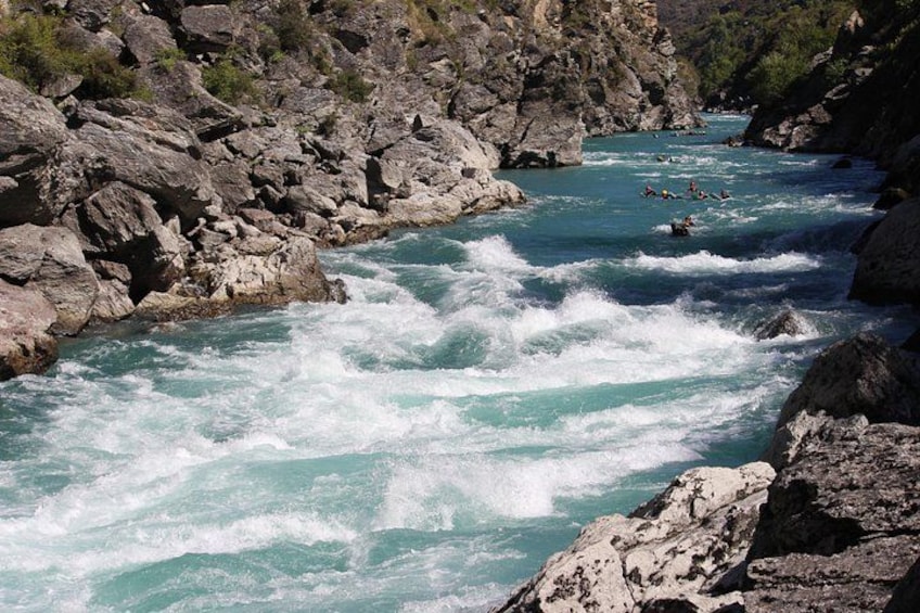 Un río turbulento con orillas rocosas y un grupo de personas haciendo rafting. 4